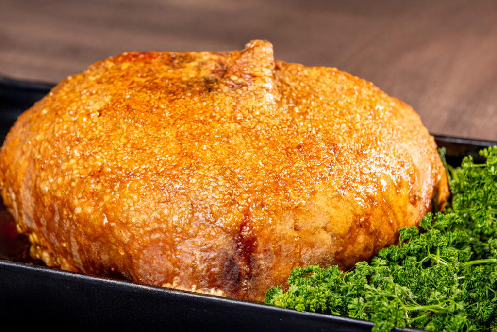 Cojín de lechona dorado sobre bandeja negra con cama de perejil fresco, ideal para eventos pequeños o reuniones familiares.